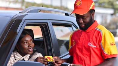 Employé Shell en uniforme remettant une carte Shell à une cliente dans sa voiture à une station-service.