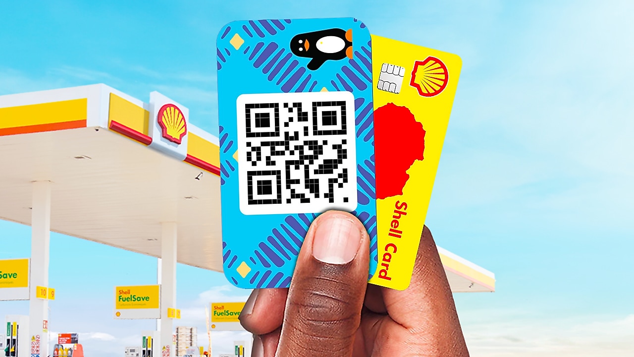 Main tenant une carte Shell et une carte Wave devant une station-service, illustrant des moyens de paiement numérique