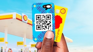 Main tenant une carte Shell et une carte Wave devant une station-service, illustrant des moyens de paiement numérique