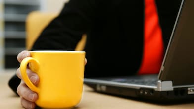 Main tenant une tasse jaune près d'un ordinateur portable sur un bureau de travail