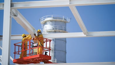 Ouvriers en tenue de protection sur une nacelle élévatrice, inspectant une structure métallique devant une tour industrielle.