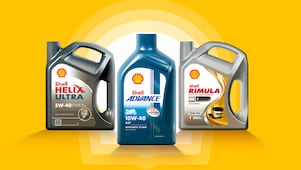 Trois bidons d’huile moteur Shell posés sur un fond jaune : à gauche Shell Helix Ultra 5W-40, au centre Shell Advance 10W-40 4T bleu pour motos, et à droite Shell Rimula 15W-40 gris pour moteurs diesel.