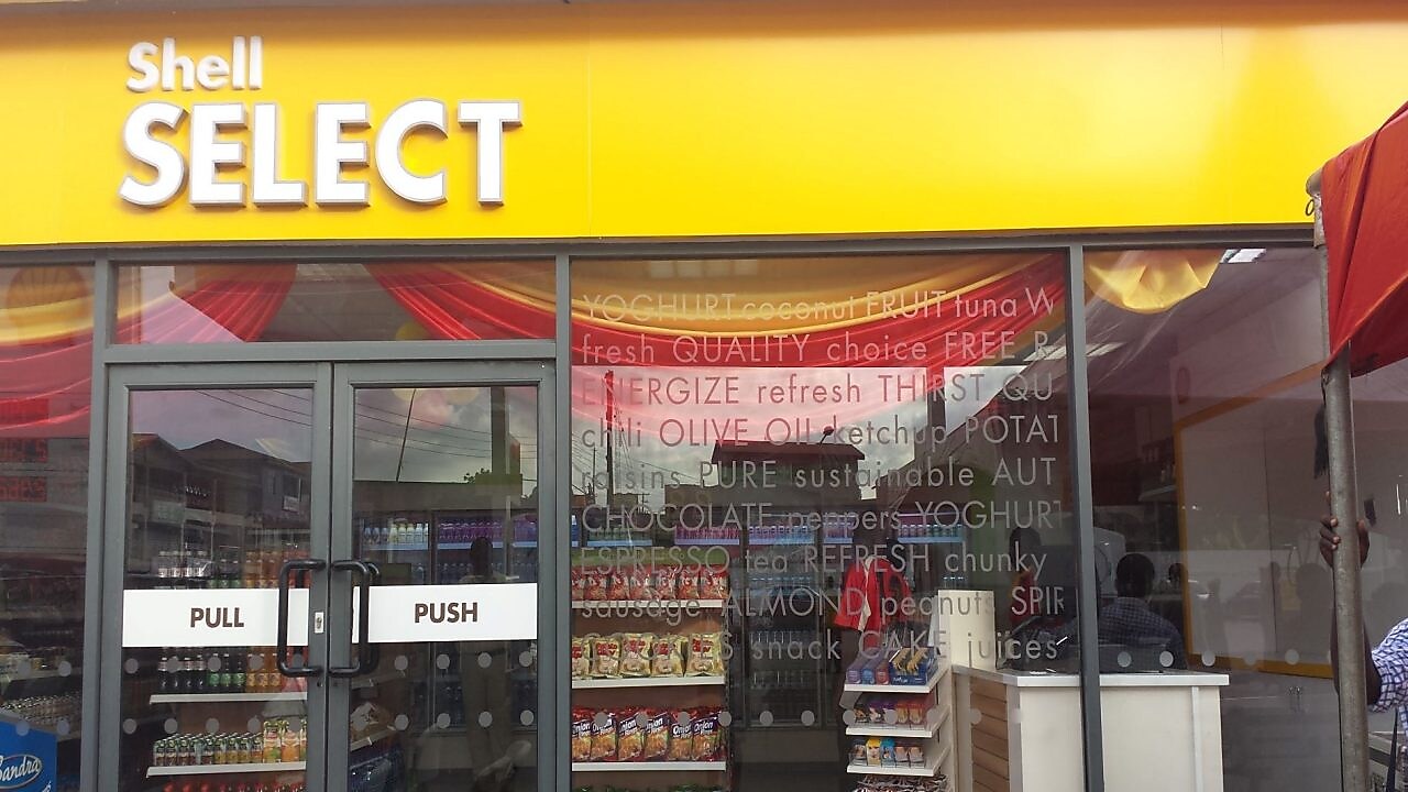 Devanture d'une boutique Shell Select avec portes vitrées et vitrine montrant des produits alimentaires et boissons