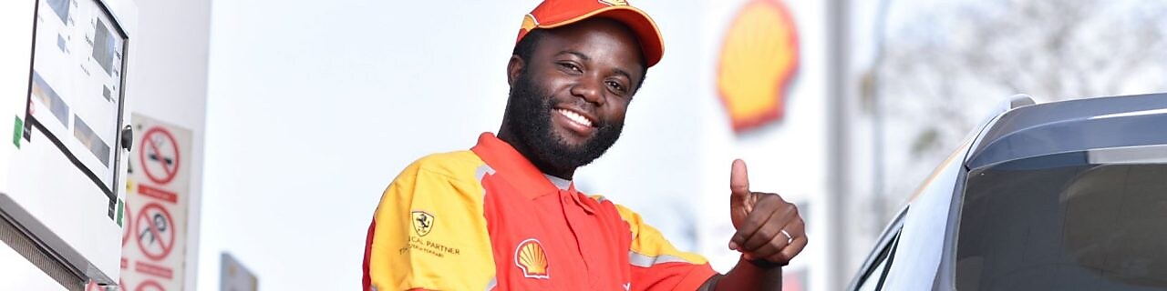 Champion de service Shell souriant en train de faire le plein de la voiture d'un client