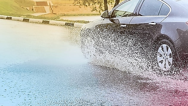 Voiture noire roulant sur route inondée, projetant des éclaboussures d'eau autour de ses roues