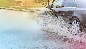 Voiture noire roulant sur route inondée, projetant des éclaboussures d'eau autour de ses roues