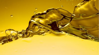 Ondulations et éclaboussures d'huile dorée en gros plan, créant des formes abstraites et liquides sur fond jaune