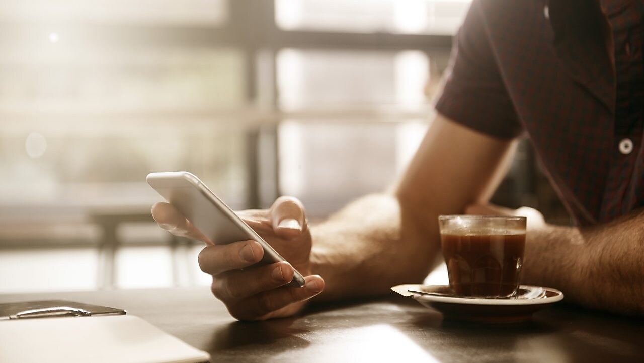 Main tenant un smartphone près d'une tasse d'espresso dans un café baigné de lumière naturelle