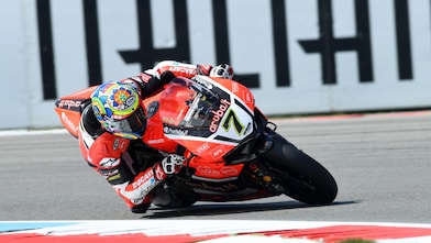 Moto Ducati rouge numéro 7 penchée dans un virage sur circuit, avec pilote portant un casque coloré