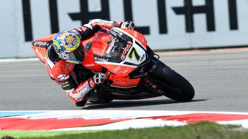 Moto Ducati rouge numéro 7 penchée dans un virage sur circuit, avec pilote portant un casque coloré