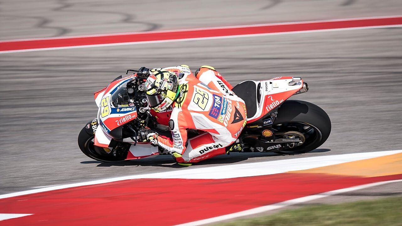 Moto Ducati rouge et blanche n°29 en plein virage sur un circuit de course aux bordures rouges et blanches.
