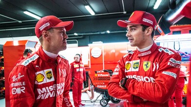 Deux pilotes Ferrari en combinaison rouge et casquette discutent dans le garage de l'équipe pendant un Grand Prix de F1
