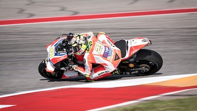 Moto Ducati rouge et blanche n°29 en plein virage sur un circuit de course aux bordures rouges et blanches.