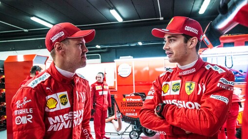 Deux pilotes Ferrari en combinaison rouge et casquette discutent dans le garage de l'équipe pendant un Grand Prix de F1