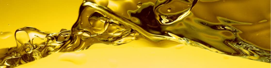 Ondulations et éclaboussures d'huile dorée en gros plan, créant des formes abstraites et liquides sur fond jaune