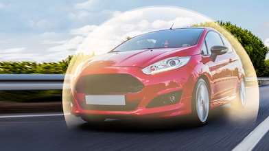 Ford Fiesta rouge en mouvement sur route, entourée d'un halo lumineux, photographiée sous un ciel bleu nuageux