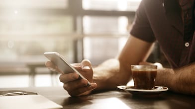 Main tenant un smartphone près d'une tasse d'espresso dans un café baigné de lumière naturelle