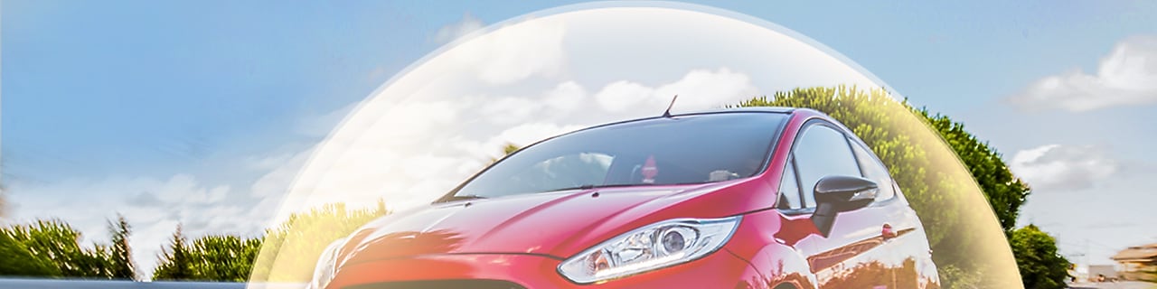 Ford Fiesta rouge en mouvement sur route, entourée d'un halo lumineux, photographiée sous un ciel bleu nuageux
