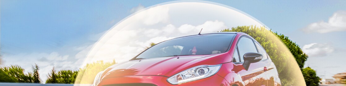 Ford Fiesta rouge en mouvement sur route, entourée d'un halo lumineux, photographiée sous un ciel bleu nuageux