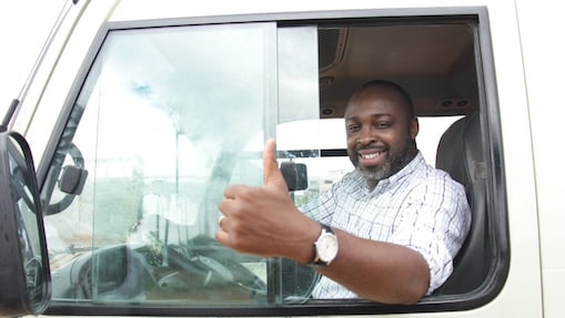 Chauffeur souriant faisant un pouce levé depuis la cabine de son camion blanc