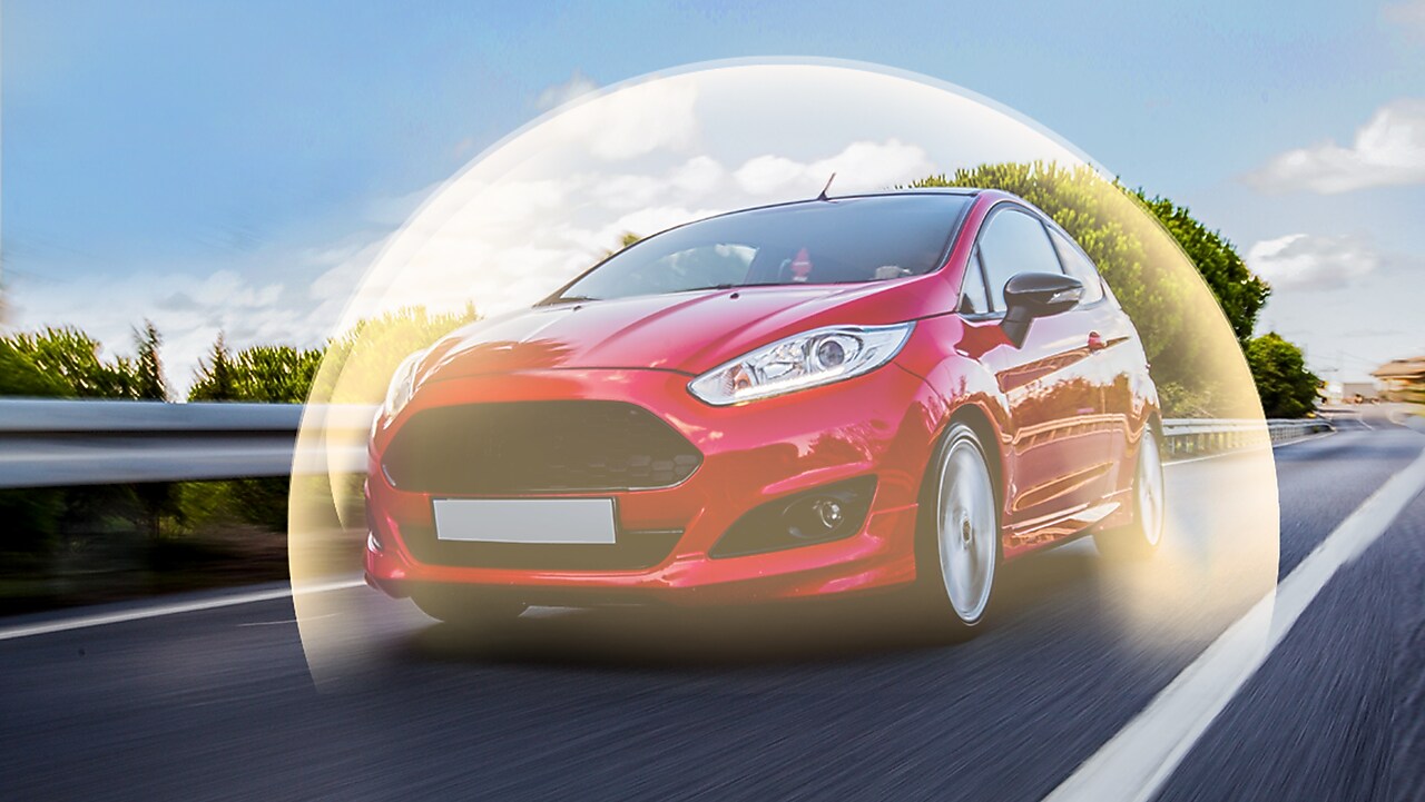 Voiture rouge Ford Fiesta en mouvement sur route, entourée d'un halo lumineux symbolisant la protection ou la sécurité