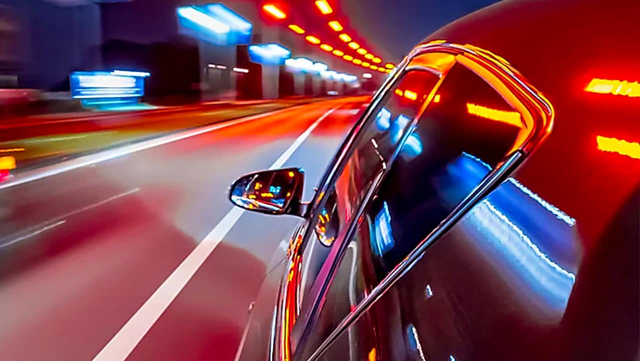 Vue dynamique d'une voiture roulant de nuit dans un tunnel illuminé de lumières rouges et bleues avec effet de vitesse.