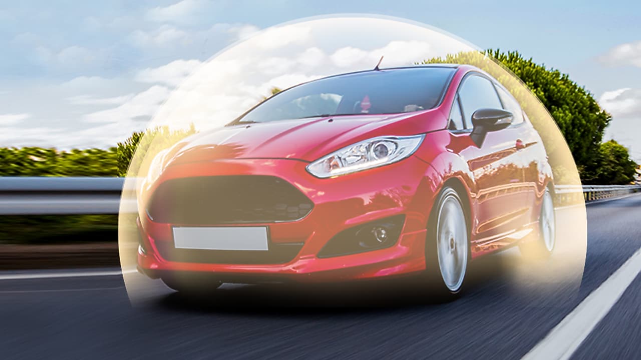 Ford Fiesta rouge en mouvement sur route, entourée d'un halo lumineux, photographiée sous un ciel bleu nuageux