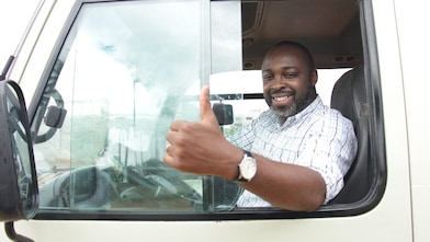 Chauffeur souriant faisant un pouce levé depuis la cabine de son camion blanc