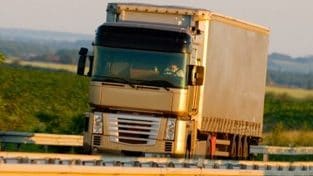 Camion semi-remorque blanc et argenté roulant sur une route rurale par une journée ensoleillée