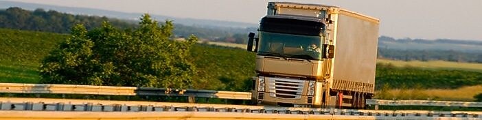 Camion semi-remorque blanc et argenté roulant sur une route rurale par une journée ensoleillée
