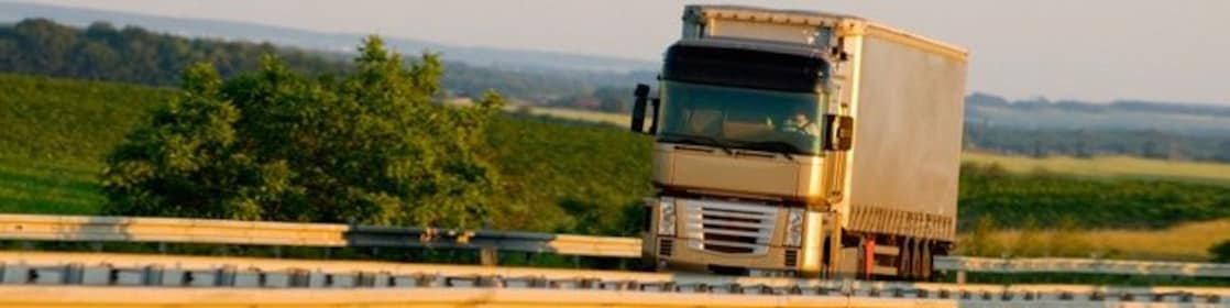 Camion semi-remorque blanc et argenté roulant sur une route rurale par une journée ensoleillée