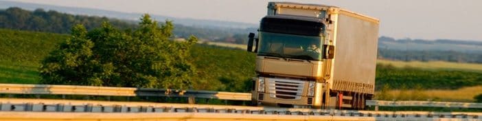 Camion semi-remorque blanc et argenté roulant sur une route rurale par une journée ensoleillée