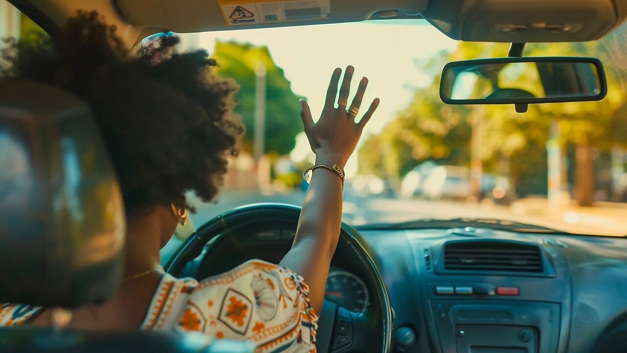 Conducteur levant la main en signe de salut depuis l'intérieur d'une voiture par une journée ensoleillée