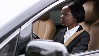 Professionnelle en tailleur noir au volant d'une voiture de luxe avec intérieur beige, vue à travers la vitre du conducteur