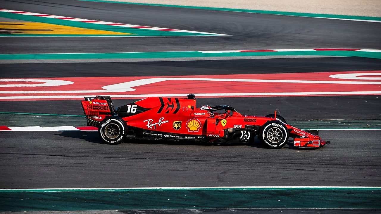 Voiture Ferrari F1 numéro 16 en action sur un circuit de course avec bordures rouge et vert