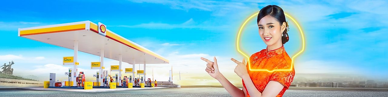 Une femme chinoise vêtue d'une robe rouge indique une station-service Shell sous un ciel bleu éclatant.