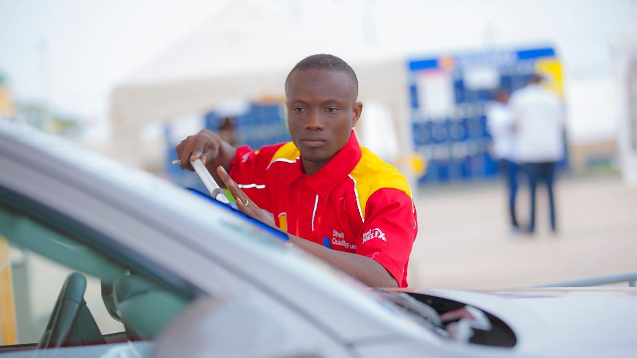 Employé de station-service en uniforme rouge Shell nettoyant le pare-brise d'une voiture