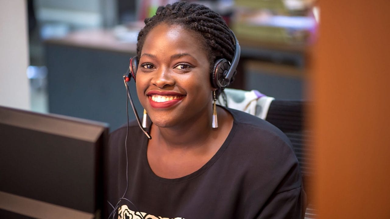 Représentante service client Shell souriante portant un casque dans un bureau, vêtue d'un haut noir.