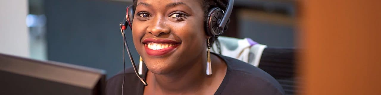 Représentante service client Shell souriante portant un casque dans un bureau, vêtue d'un haut noir.