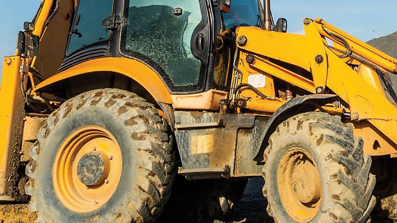 Gros plan sur les roues et la cabine d'un tractopelle jaune couvert de boue sur un chantier de construction.