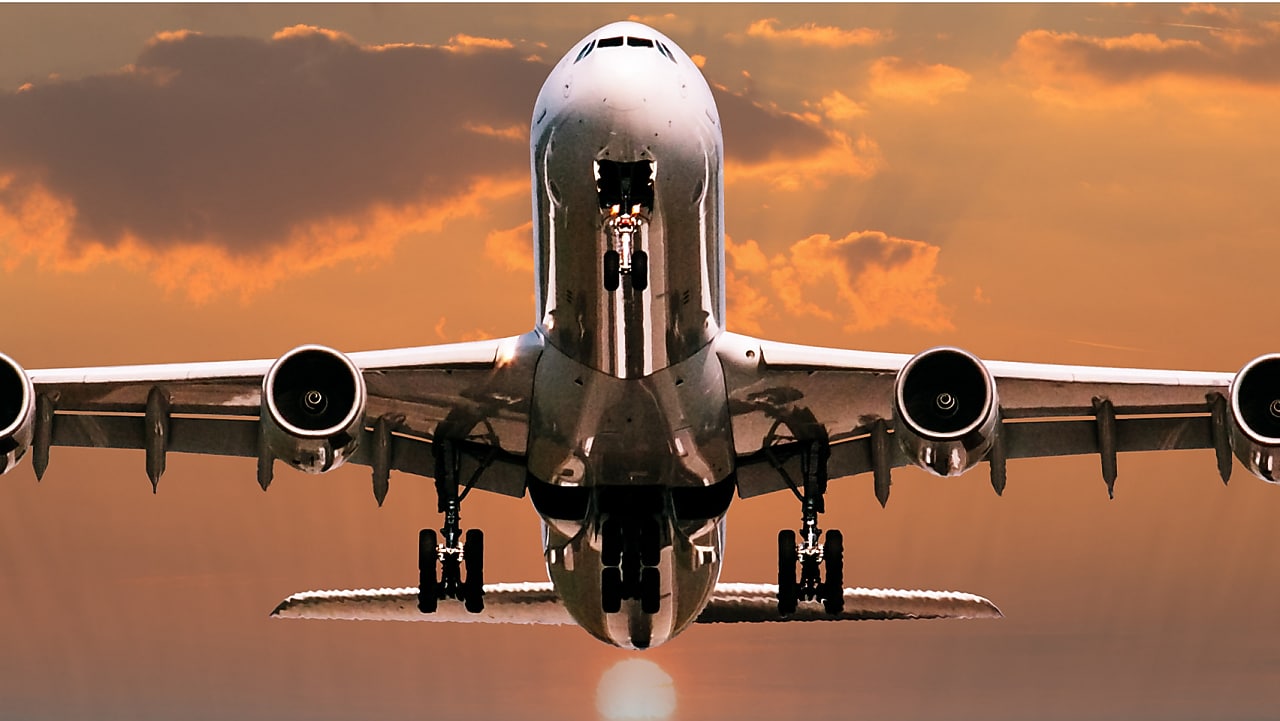 Avion commercial gros-porteur photographié de face au coucher du soleil, avec un ciel orange dramatique en arrière-plan.