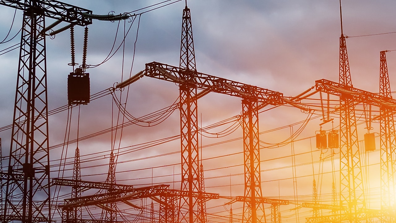 Pylônes et lignes électriques à haute tension au coucher du soleil, créant une silhouette industrielle contre un ciel orangé.