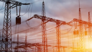 Pylônes et lignes électriques à haute tension au coucher du soleil, créant une silhouette industrielle contre un ciel orangé.