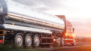 Camion-citerne en acier inoxydable brillant roulant au coucher du soleil, transportant des liquides sur une route