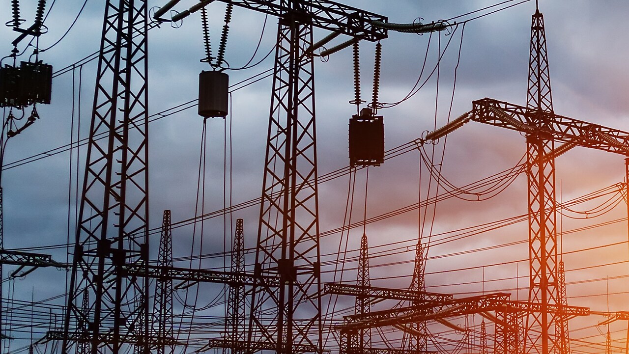 Pylônes et lignes électriques à haute tension au coucher du soleil, créant une silhouette industrielle contre un ciel orangé.