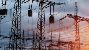 Pylônes et lignes électriques à haute tension au coucher du soleil, créant une silhouette industrielle contre un ciel orangé.