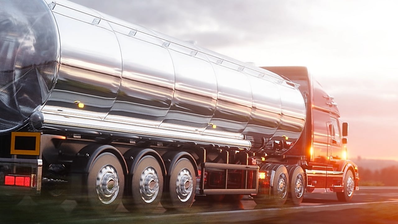 Camion-citerne en acier inoxydable brillant roulant au coucher du soleil, transportant des liquides sur une route